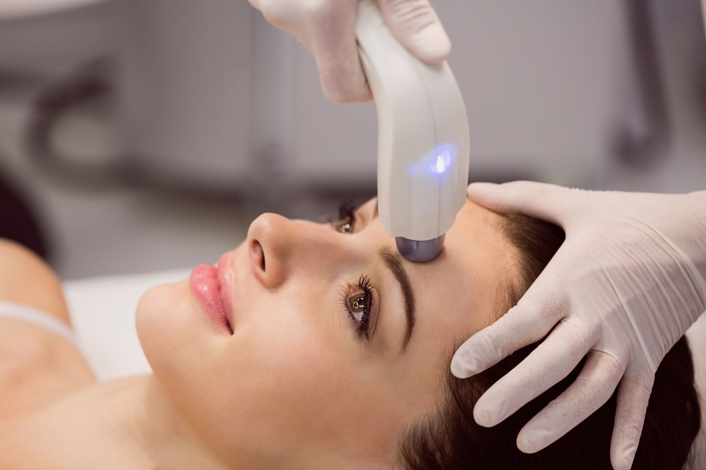 A imagem apresenta um procedimento estético facial sendo realizado em uma paciente que está deitada e relaxada, enquanto um profissional utiliza um dispositivo avançado de ultrassom microfocado na região da testa.