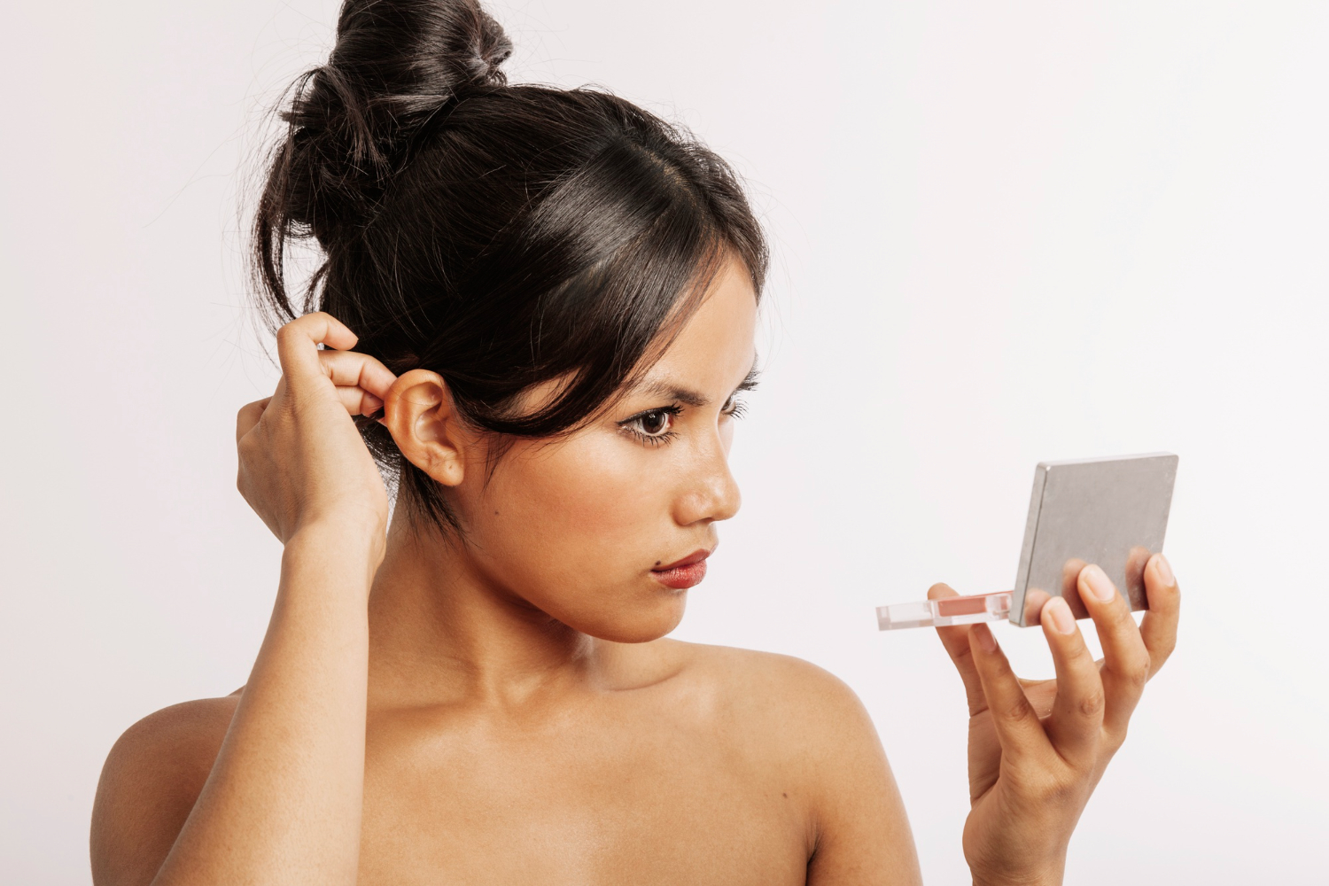 Jovem mulher avaliando suas orelhas em espelho de mão, representando consulta de otomodelação para correção estética de orelhas de abano sem cirurgia