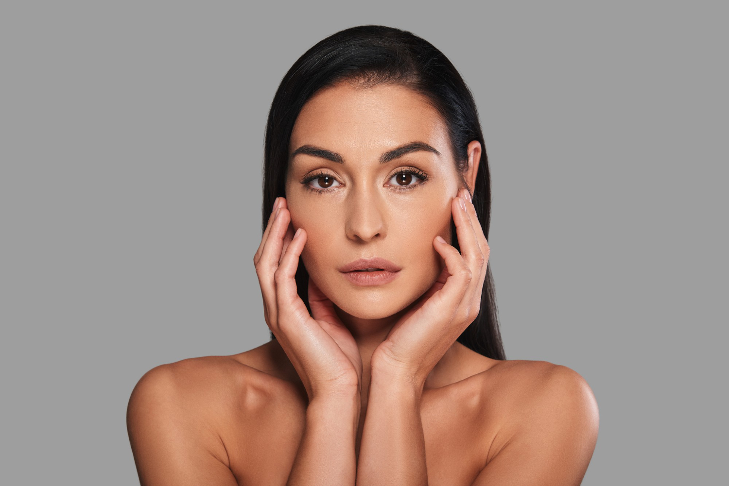 Mulher com pele saudável e luminosa tocando o rosto, representando resultado natural de harmonização facial equilibrada com preenchimentos que respeitam a individualidade e proporcionam equilíbrio estético.