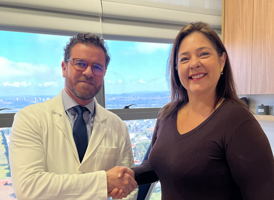 Dr. Paulo Junqueira cumprimenta a paciente Vanessa Faro com um aperto de mãos em consultório, em contexto de acompanhamento médico voltado à gestão do envelhecimento facial.